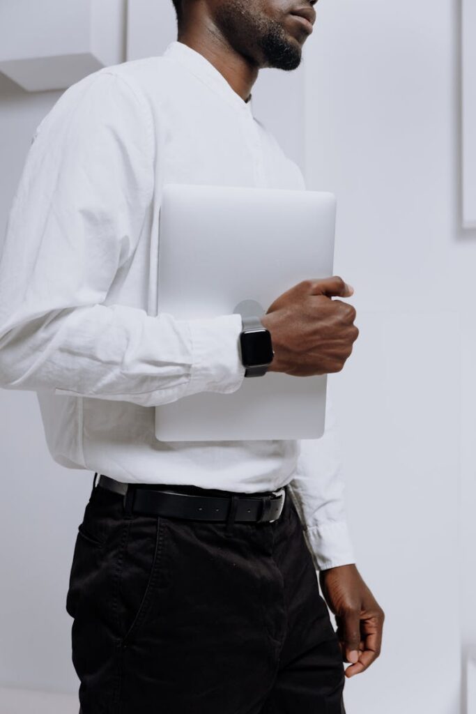 A man in a white shirt holding a laptop while wearing a smartwatch in a modern office setting.